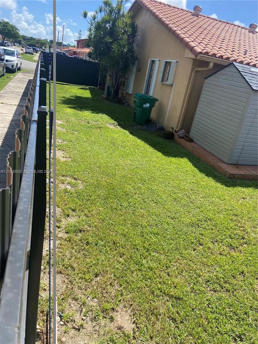 Tiled roof structure with stucco exterior, a side yard featuring a lawn, and a privacy fence