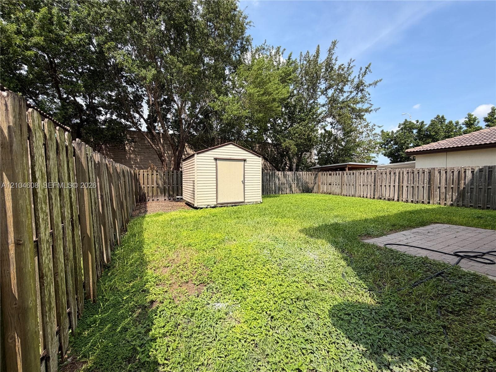 Rear yard featuring a wood fence, storage shed, paver patio, and mature trees