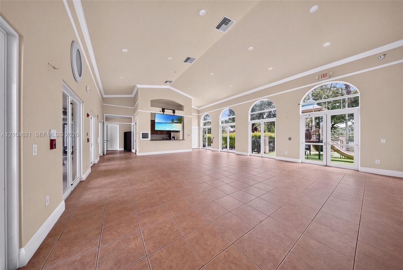 Expansive interior space featuring ceramic tile flooring, vaulted ceilings with recessed lighting, crown molding, a built-in refreshment bar with cabinetry, and multiple arched glass-paned double doors