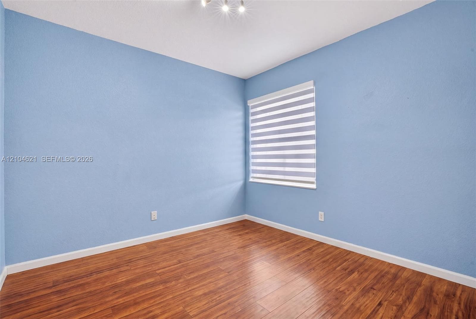 Interior room featuring wood-finish flooring, light blue textured walls, and horizontal zebra-style window shades