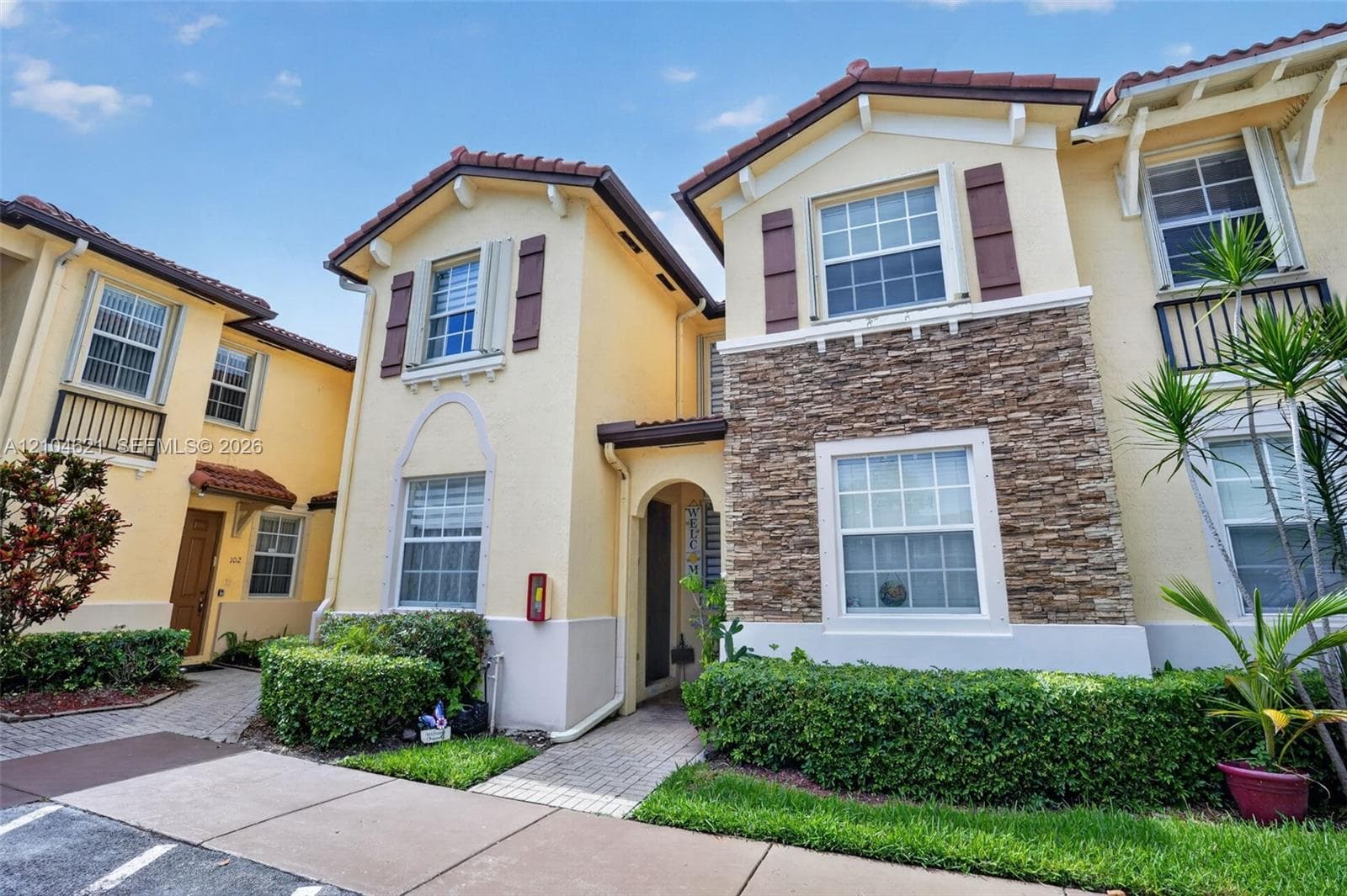 Multi-story exterior featuring a stone veneer facade, tile roofing, decorative shutter accents, iron-railed balconies, and paver walkways