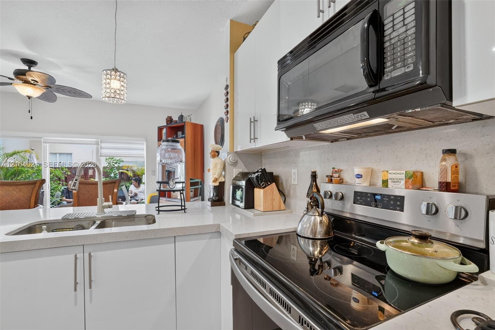 Kitchen featuring white flat-panel cabinetry, light-toned stone-finish countertops, stainless steel appliances, dual-basin sink with gooseneck faucet, and a contemporary pendant light fixture