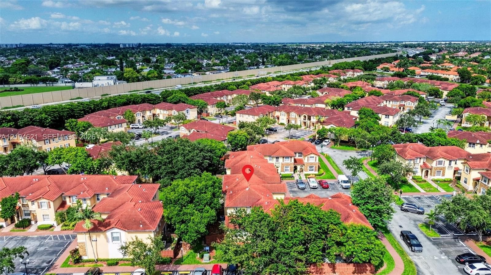 Aerial perspective of a multi-unit residential community featuring terracotta-style roofing, paved parking areas, and mature landscaping