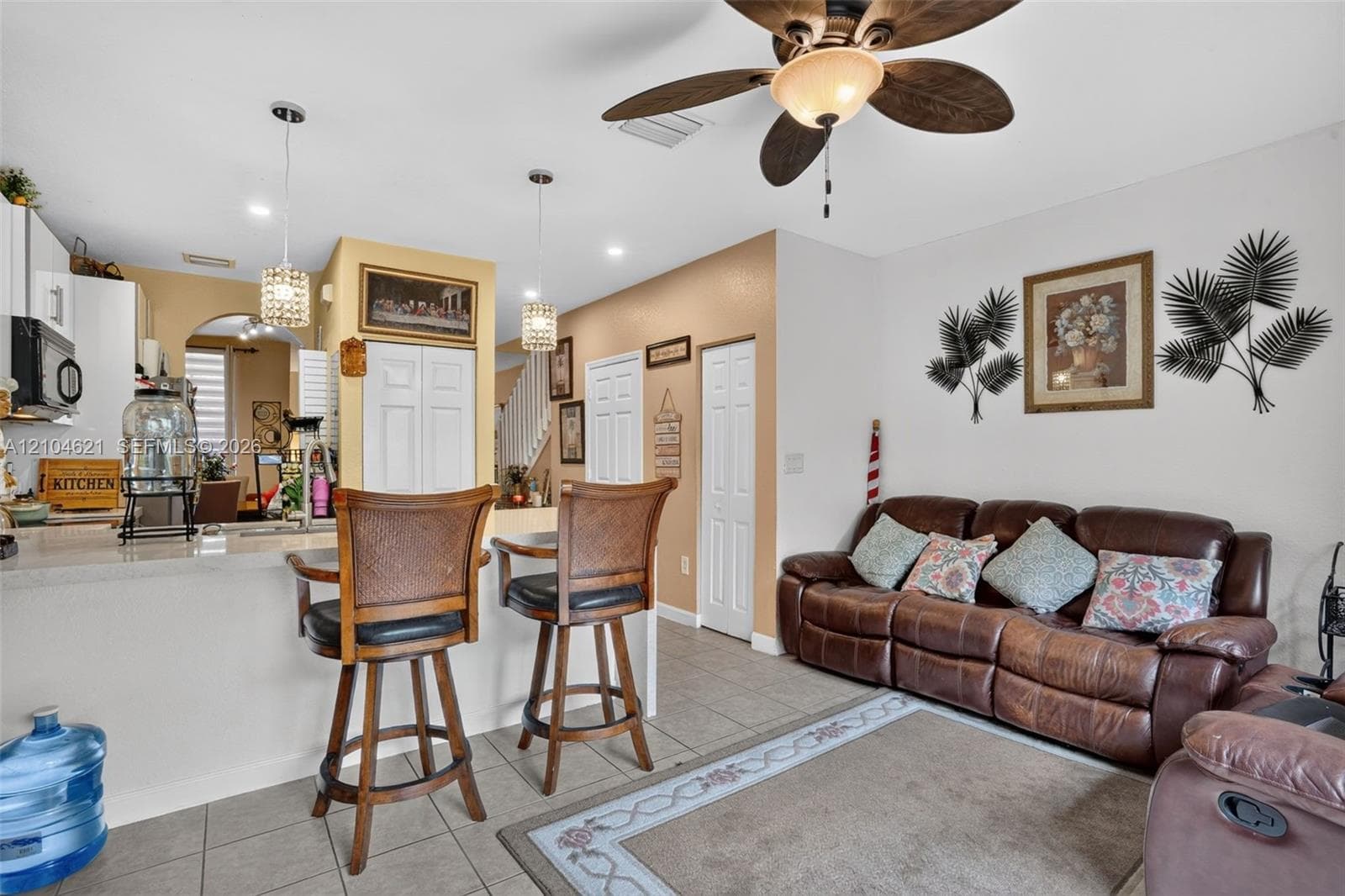 Kitchen featuring a breakfast bar with stone-finish countertop, dual pendant lighting, ceiling fan with light kit, and neutral tile flooring