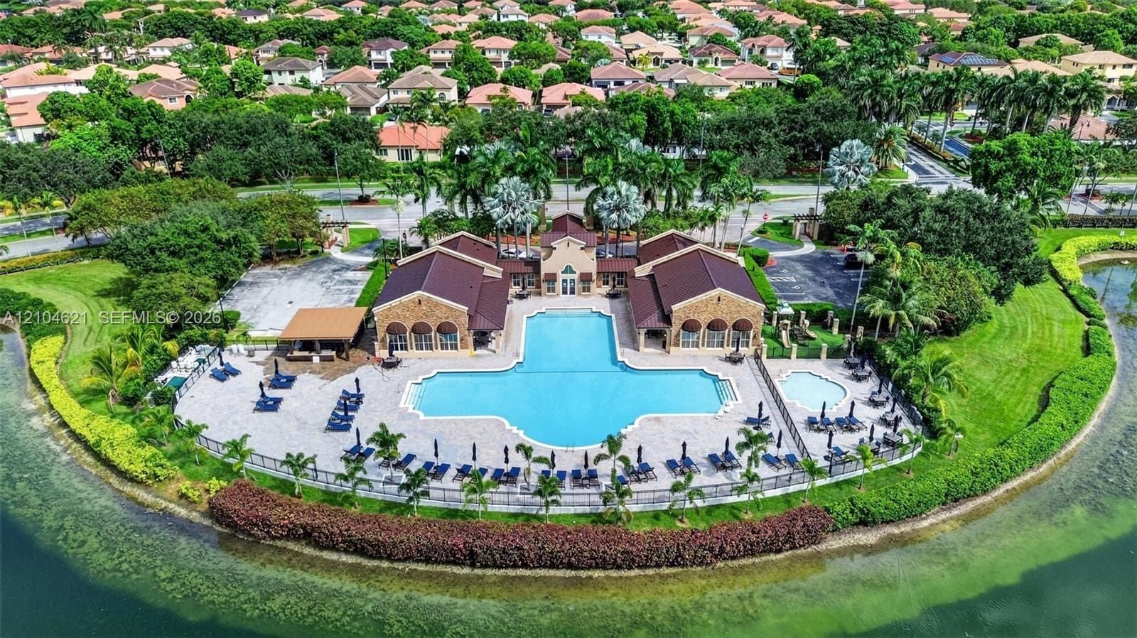 Community clubhouse featuring an expansive swimming pool, a separate spa, a shaded pavilion, and stone-paver decking, all situated along the waterfront