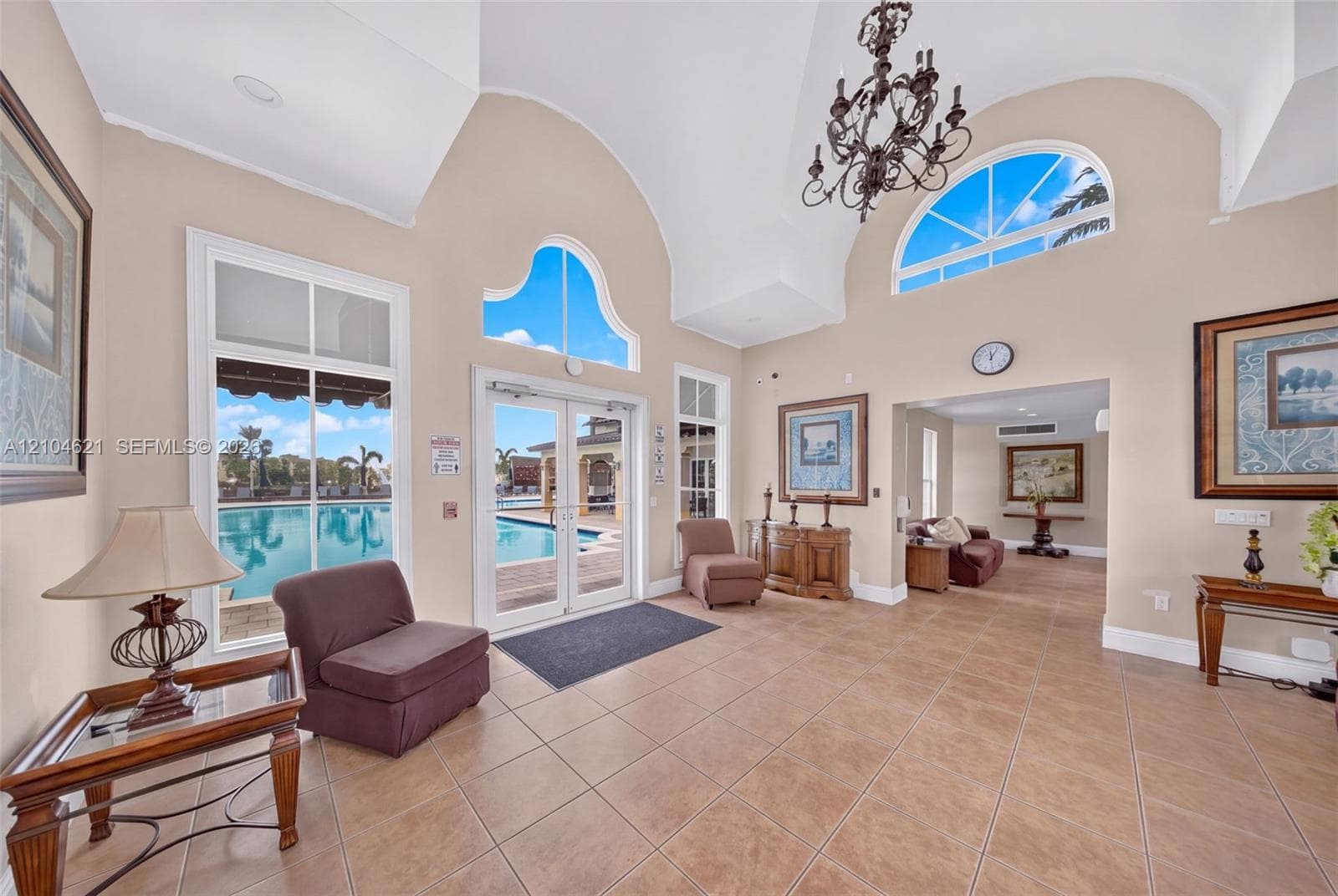 Vaulted ceilings featuring decorative arched windows and an ornate chandelier, complemented by tile flooring and double glass doors