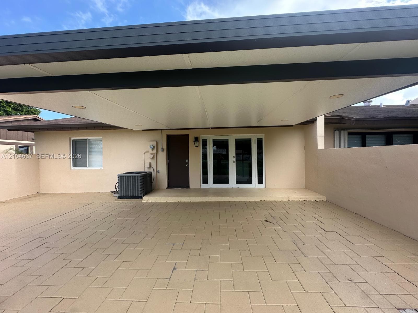Covered exterior area featuring a light-colored stucco exterior, a dark brown entry door, and double glass doors