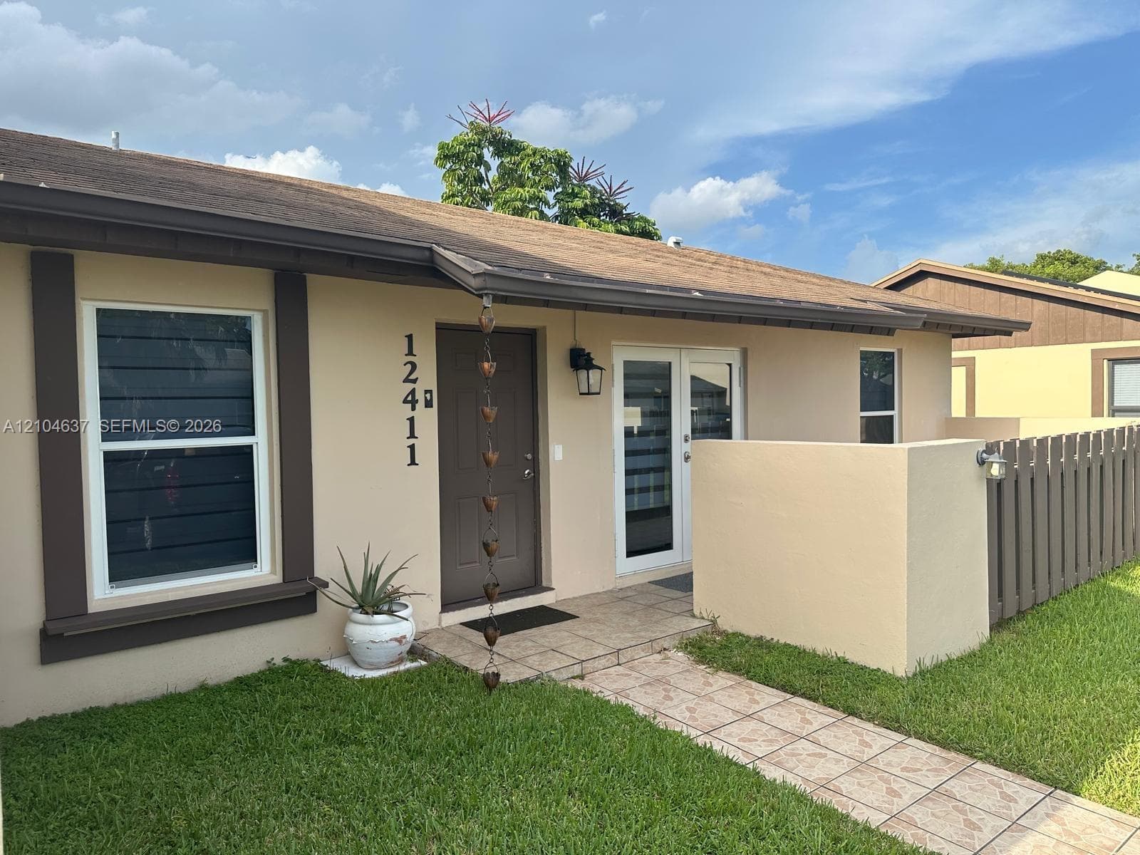 Stucco exterior with brown trim, covered front entry, tiled walkway, double-pane windows, and wood fencing