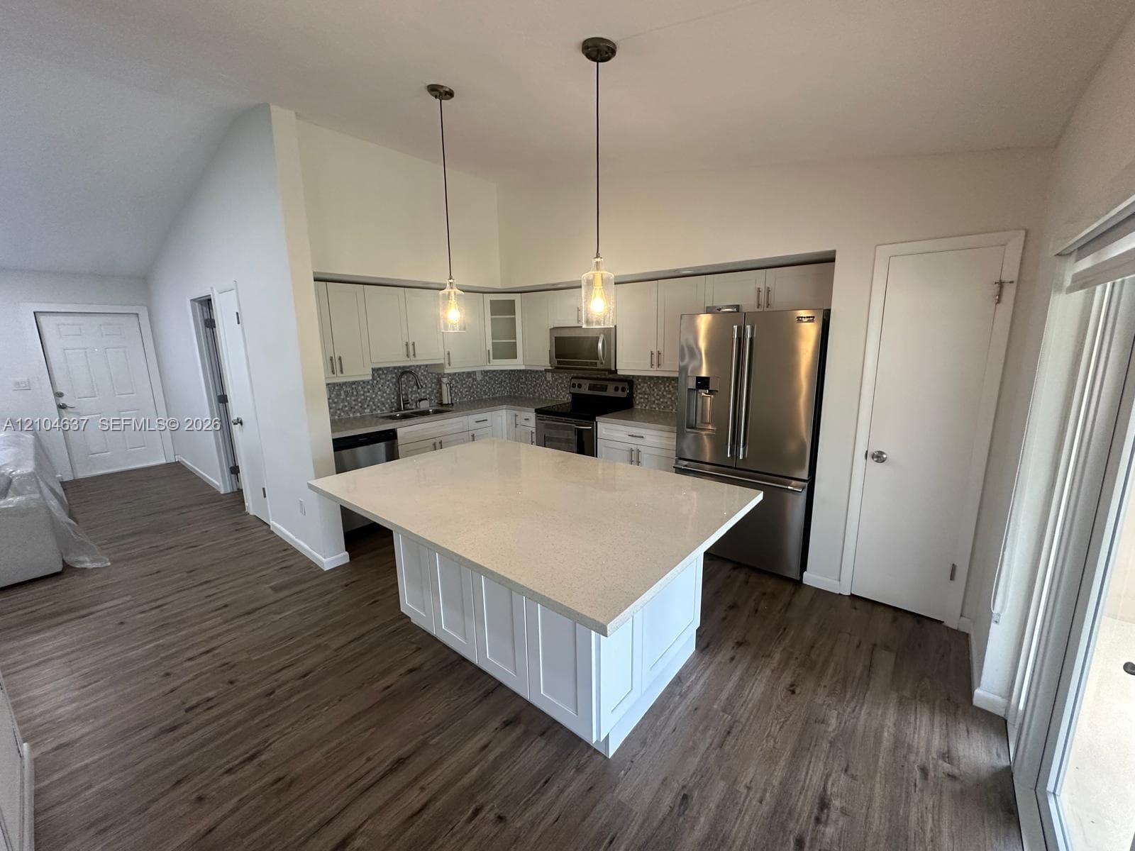 Vaulted ceilings, wood-finish flooring, white shaker cabinetry, stainless steel appliances, and a kitchen island with pendant lighting