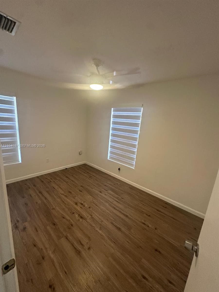 Wood-finish flooring, white walls, two windows with horizontal blinds, and a ceiling fan with integrated lighting