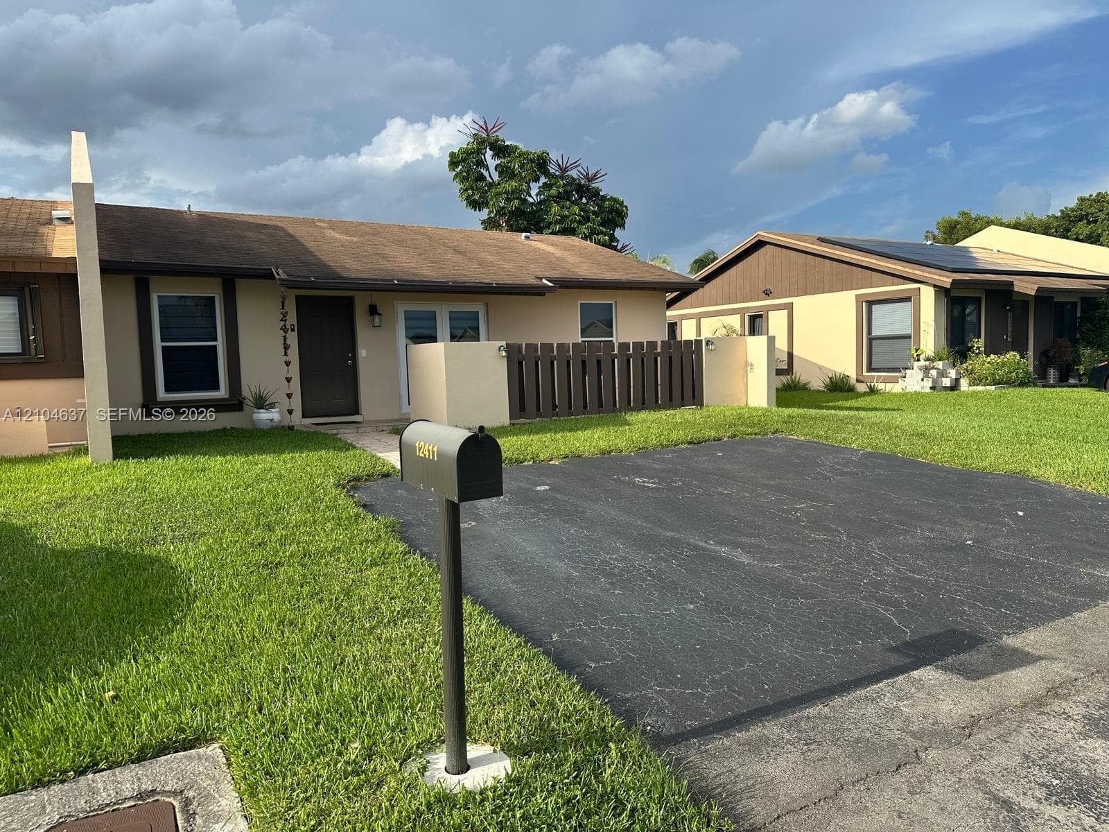 Tan exterior with brown trim, featuring a dark asphalt driveway and a manicured lawn