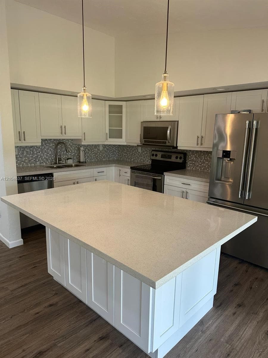 Kitchen featuring a spacious island with light-toned countertop, white cabinetry, stainless steel appliances, and wood-finish flooring