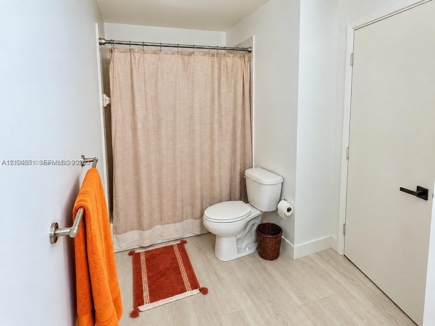 Bathroom featuring wood-finish flooring, a two-piece toilet, and a shower-tub combination with a metal curtain rod and hardware