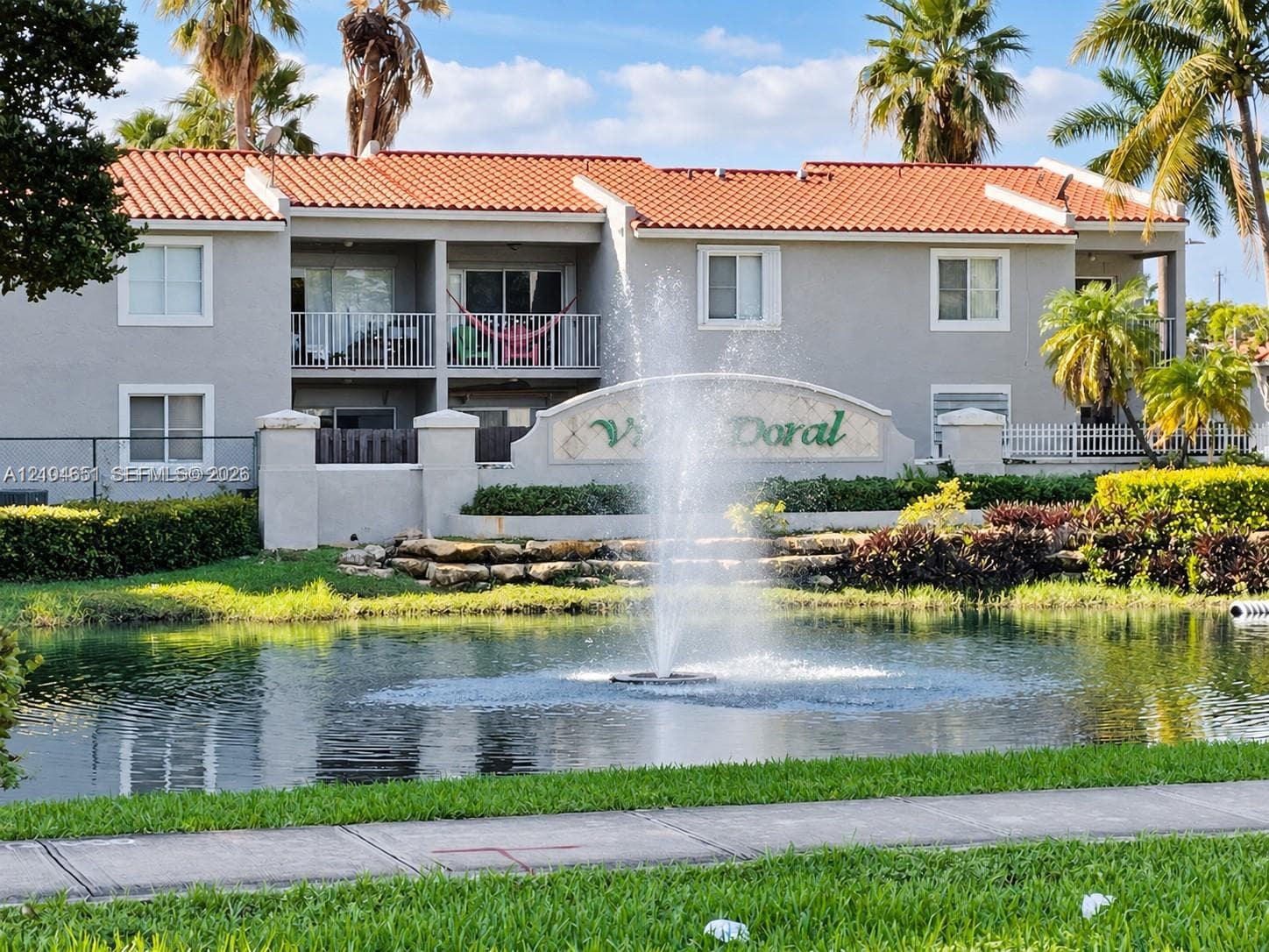 Multi-story building featuring a tile roof, stucco exterior, private balconies, and a central water fountain situated within a pond