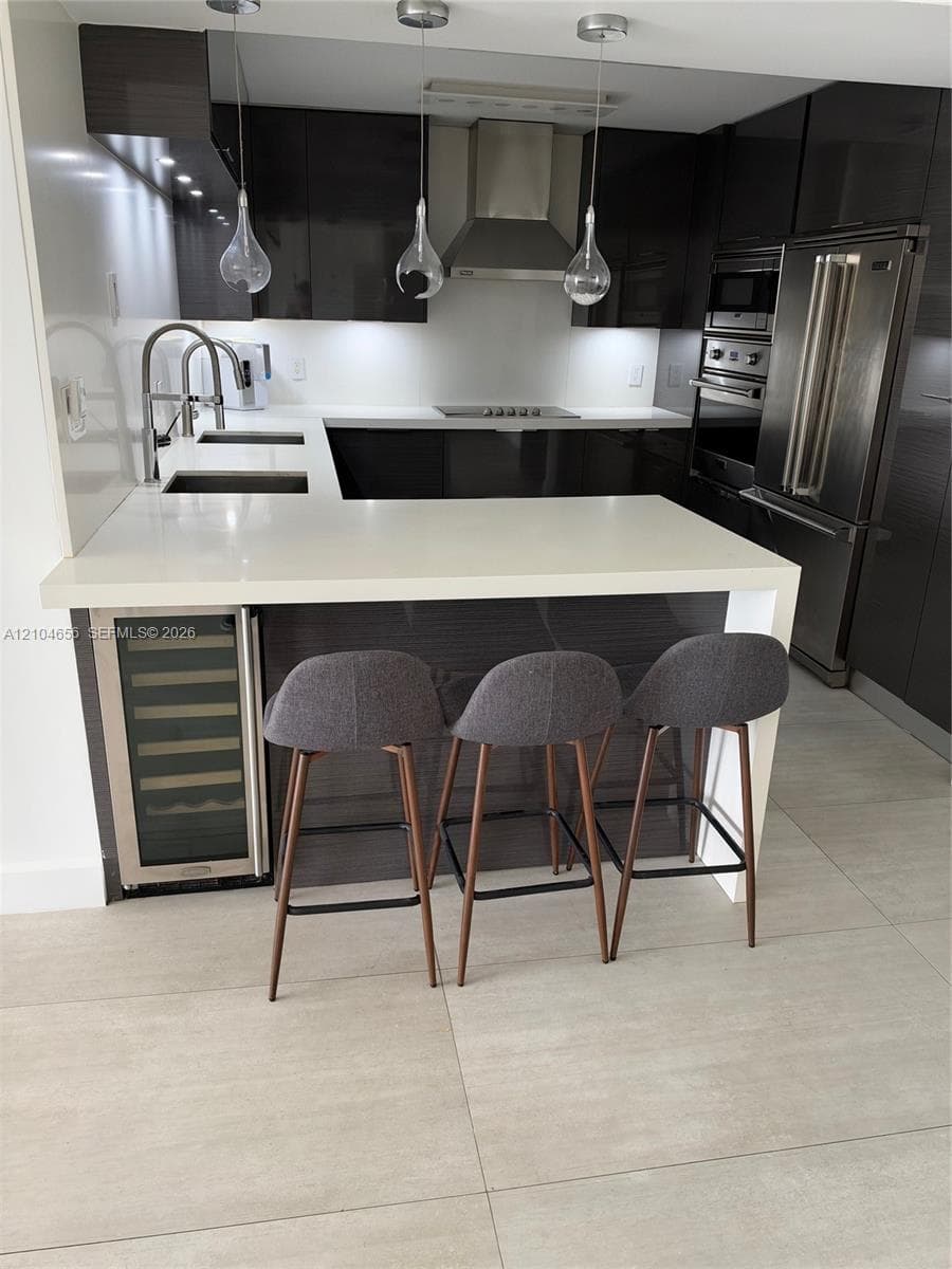 Modern kitchen featuring high-gloss cabinetry, stone-surface breakfast bar, integrated wine refrigerator, stainless steel appliances, and pendant lighting