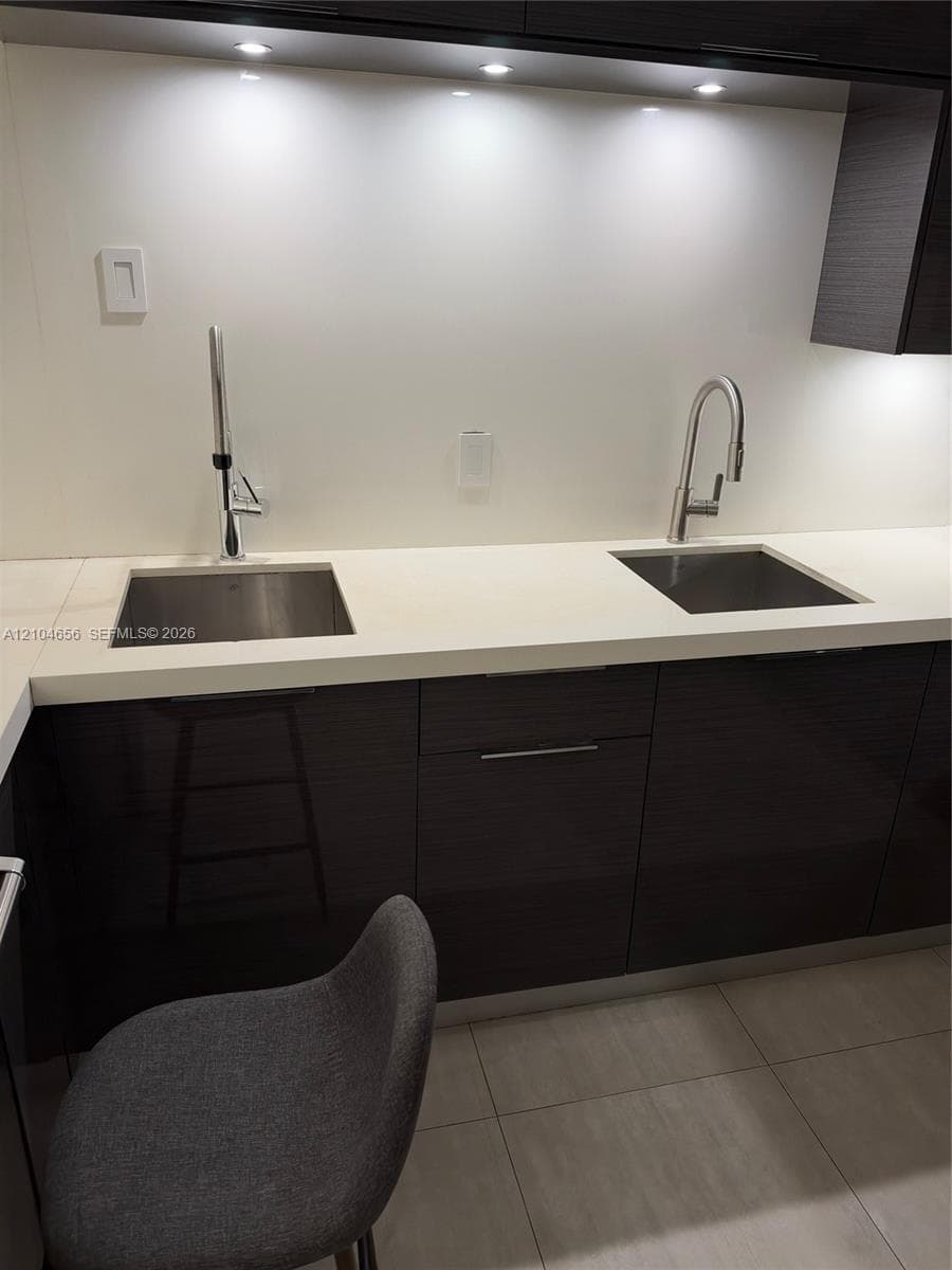Dual stainless steel under-mount sinks with high-arc gooseneck faucets, smooth white countertops, and dark, high-gloss cabinetry with recessed lighting