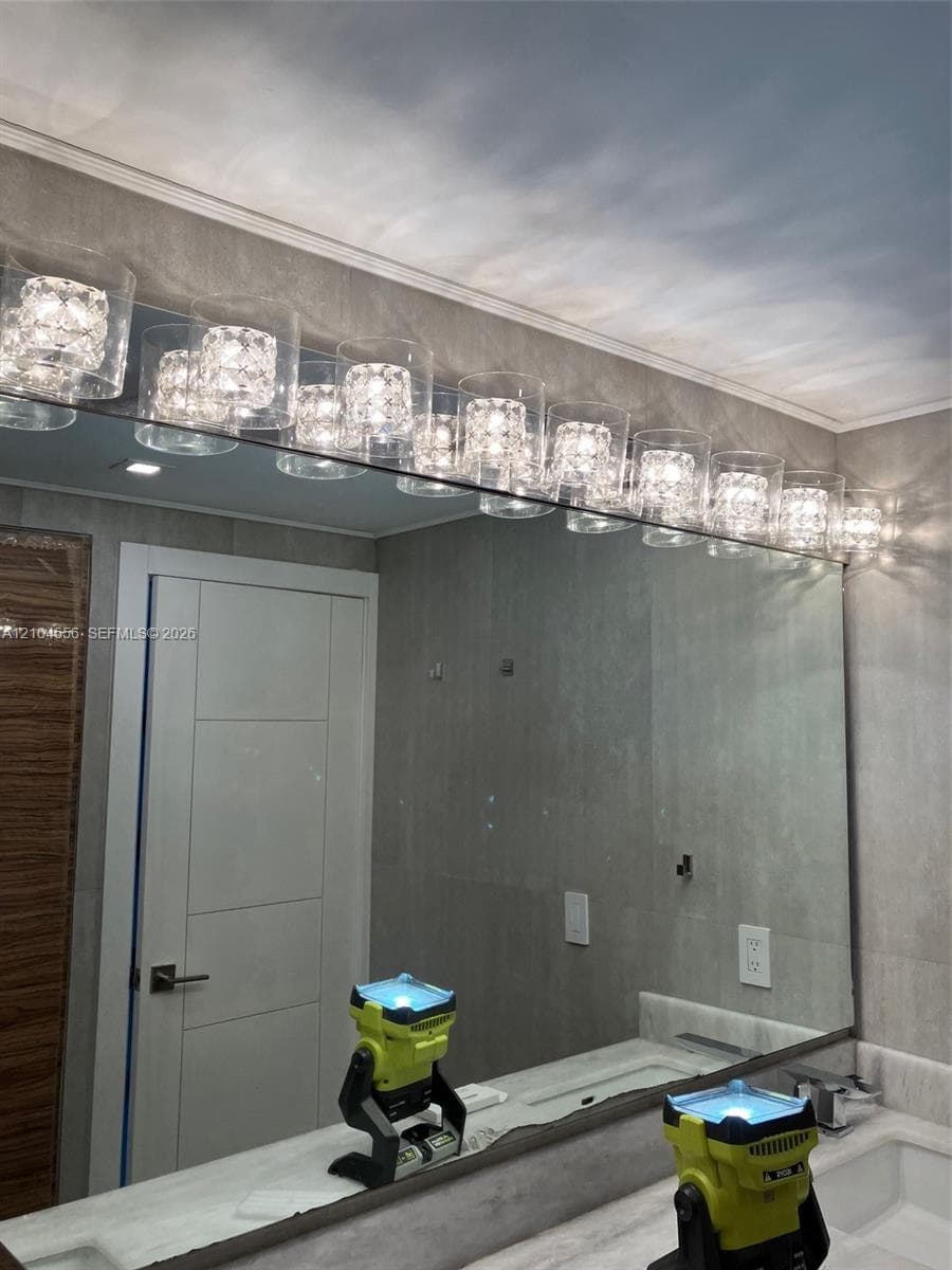 Full-width vanity mirror featuring a multi-light fixture with cylindrical glass shades, complemented by large-format gray wall tiling and a white countertop with an integrated basin