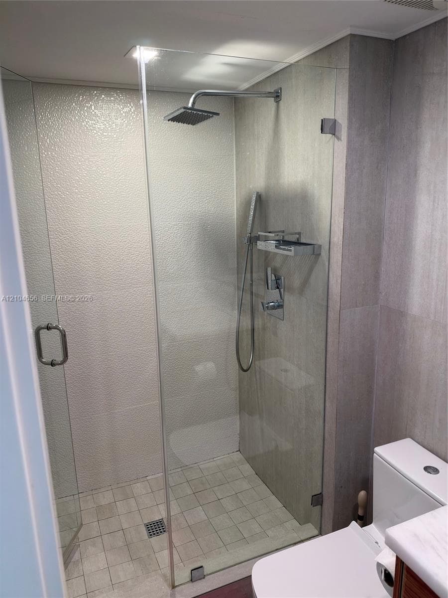 Walk-in shower featuring a frameless glass enclosure, rainfall showerhead, integrated handheld sprayer, and stone-finish tile surround