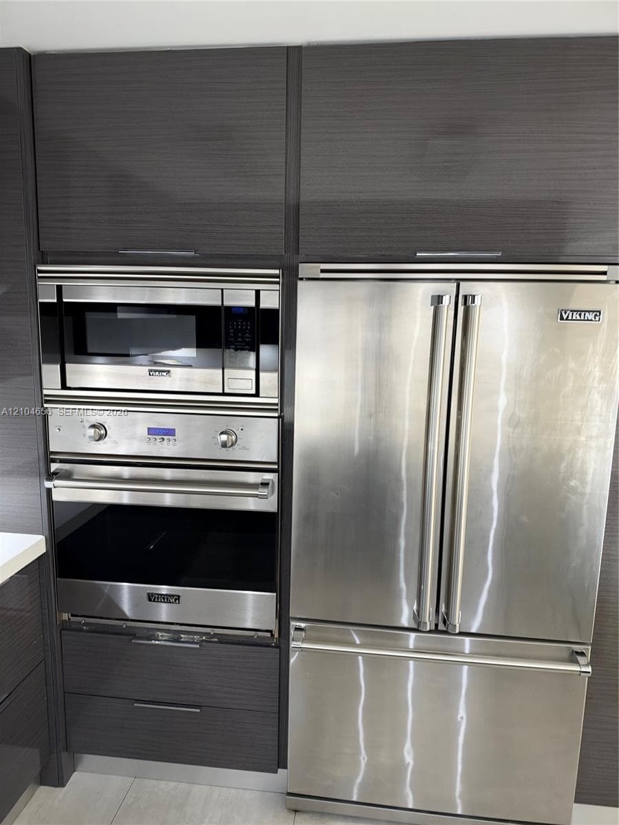 High-gloss, dark-toned cabinetry featuring integrated stainless steel Viking appliances, including a French-door refrigerator, a built-in microwave, and a wall oven