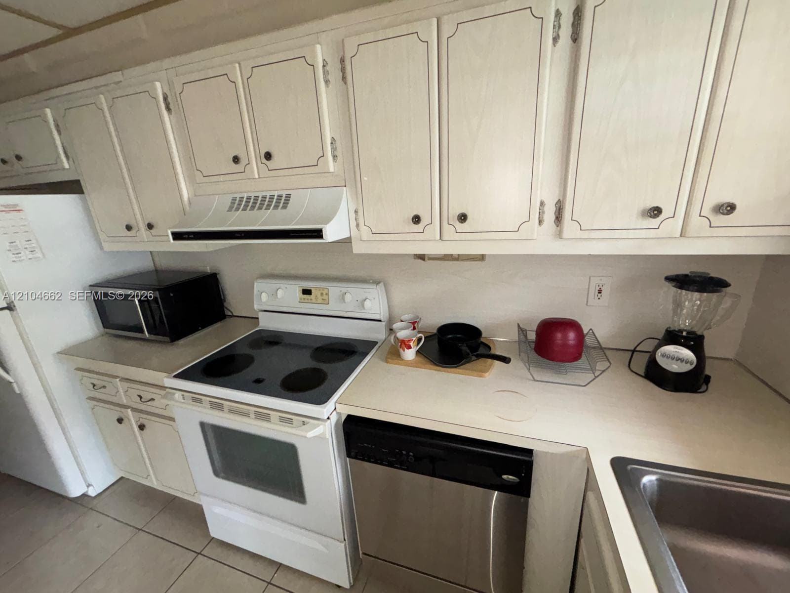 White cabinetry, light-toned countertops, white range with overhead vent, and a stainless steel dishwasher