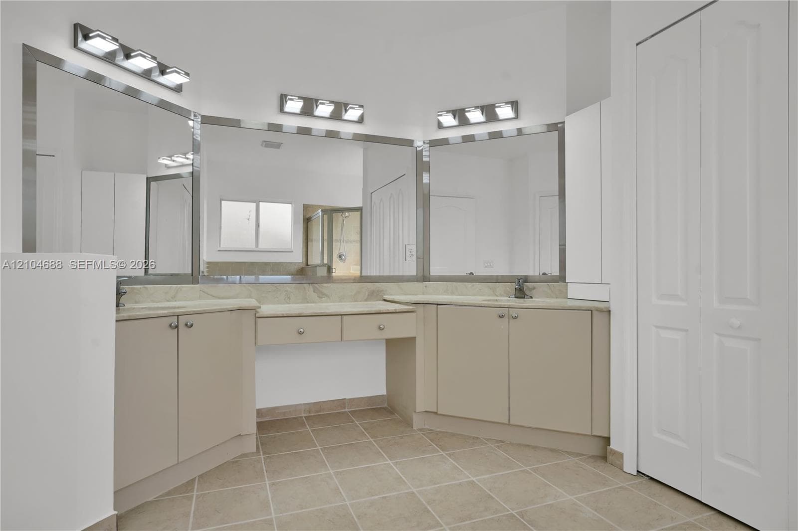 Dual-sink vanity with stone countertop, central built-in vanity station, three triple-light wall-mounted fixtures, expansive plate-glass mirrors, and tile flooring