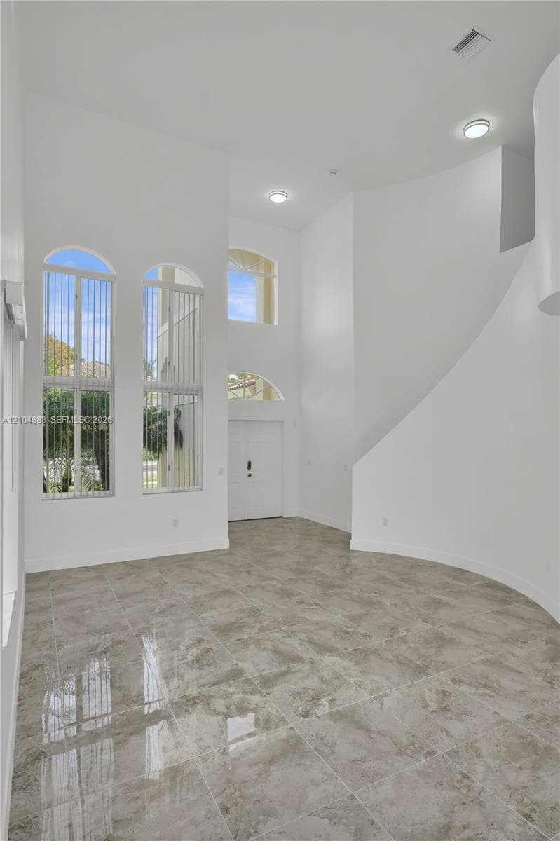 High-ceilinged entry featuring stone-finish tile flooring, arched windows, recessed lighting, and a curved architectural wall
