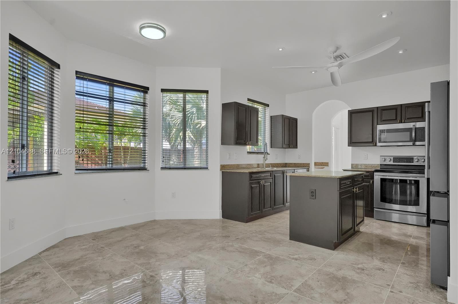 Kitchen featuring dark-toned cabinetry, stone countertops, a central island, stainless steel appliances, and tile flooring