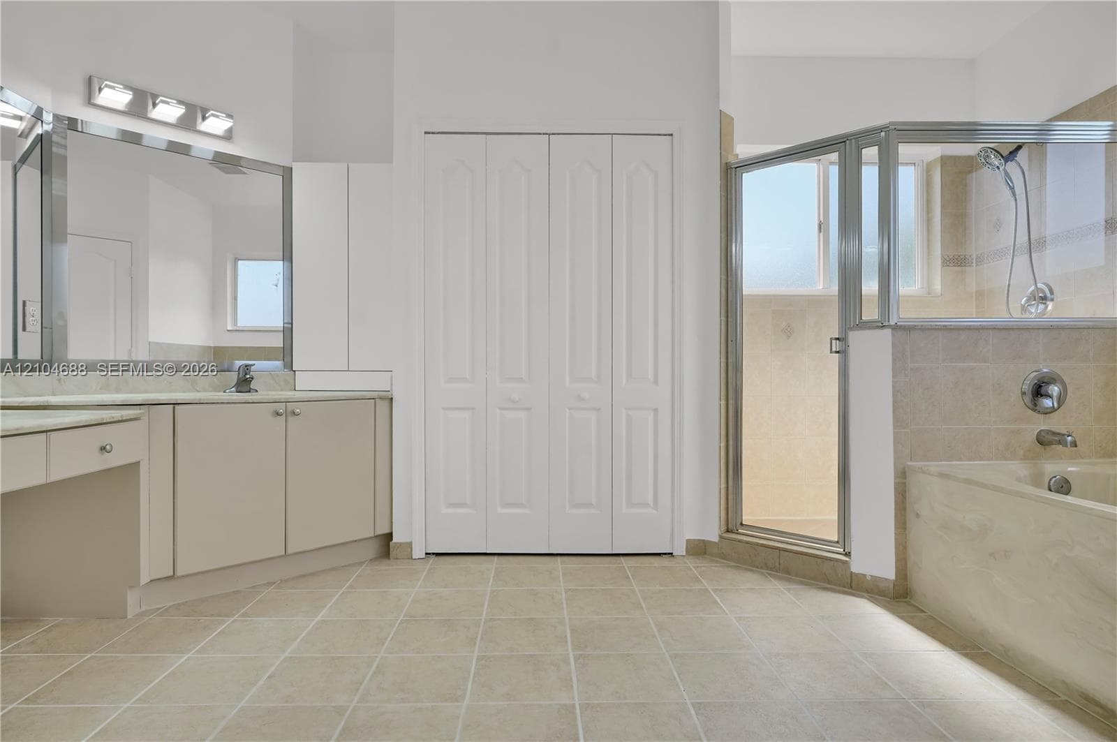 Bathroom featuring a vanity with a large mirror, a tiled soaking tub, a glass-enclosed shower, tile flooring, and floor-to-ceiling bi-fold closet doors