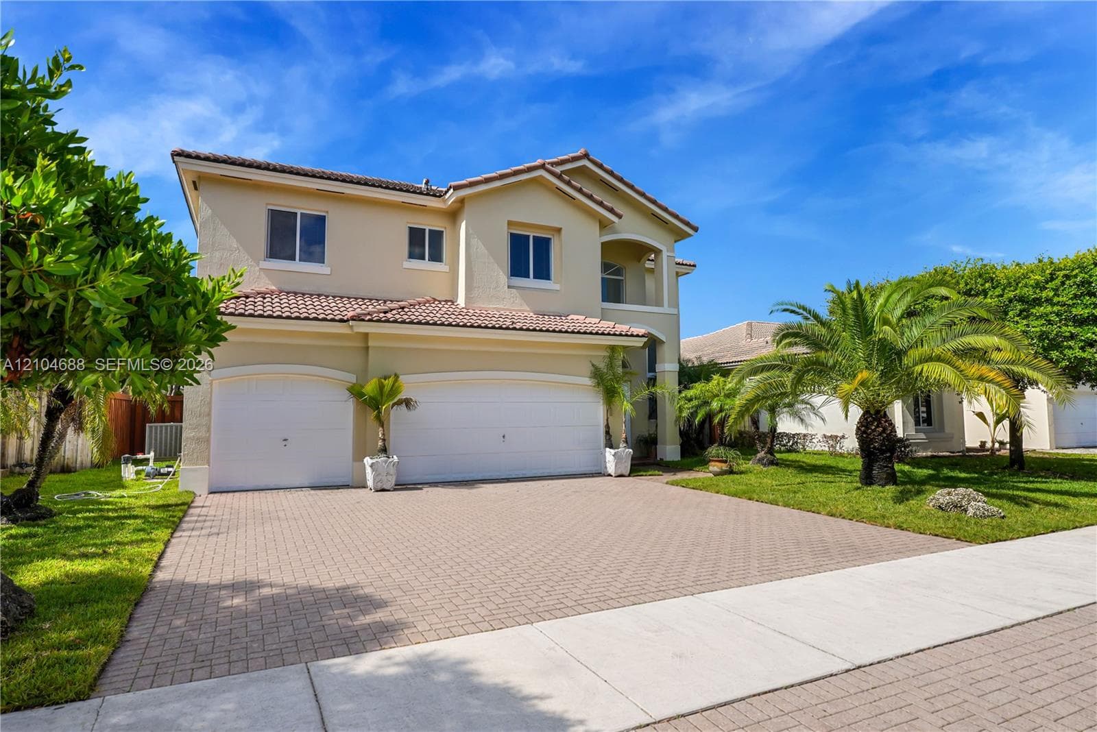 Two-story exterior featuring a beige stucco facade, a multi-car garage with arched entryways, a tile roof, and a paved driveway