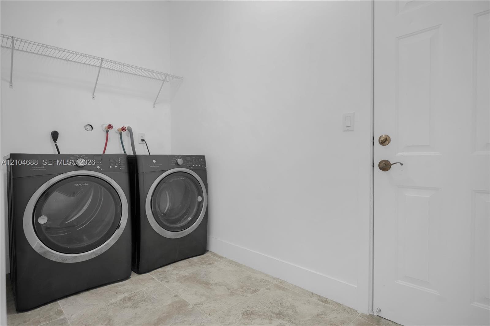 Utility area featuring tile flooring, white interior door with brass-finish hardware, and mounted wire shelving