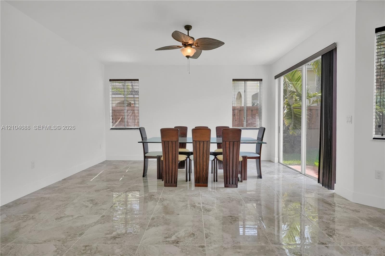 Large-format polished stone flooring, sliding glass patio doors, and a decorative ceiling fan with integrated lighting