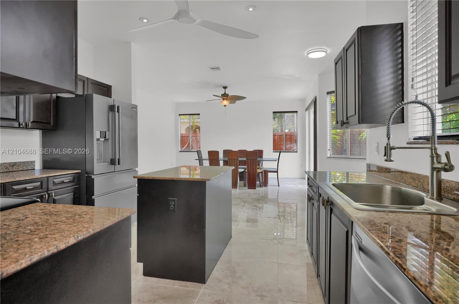 Kitchen featuring dark-finish cabinetry, stone countertops, stainless steel appliances, a center island, and tile flooring