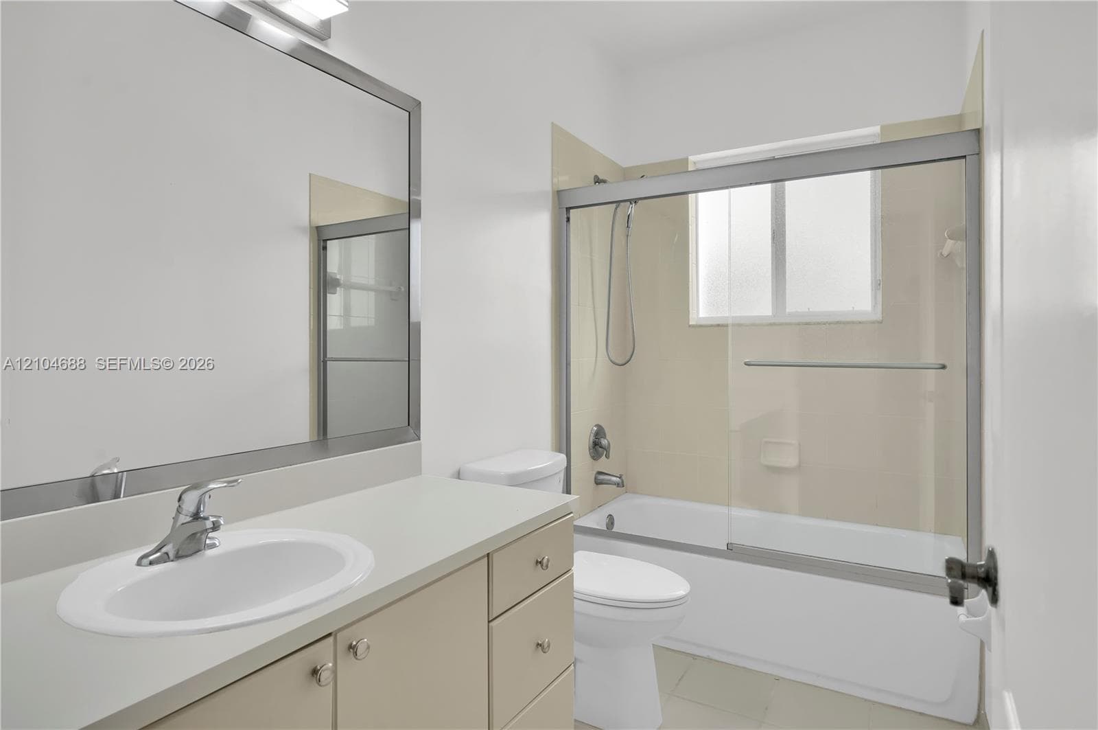 Bathroom featuring a solid-surface countertop with an integrated basin, large-format mirror with a metallic frame, vanity cabinet storage, and a bathtub with a sliding glass enclosure