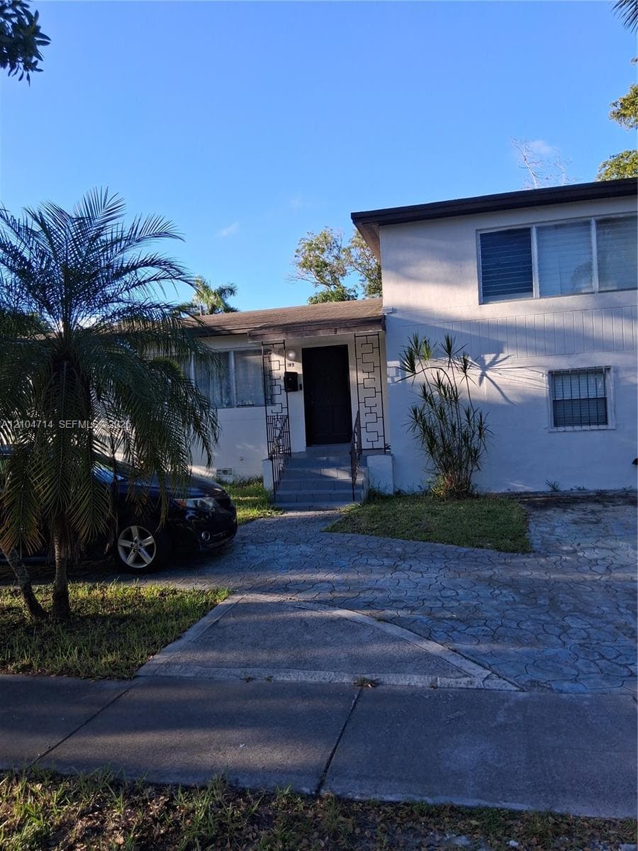 Stucco exterior with a flat roof, featuring a textured concrete driveway and mature palm tree landscaping