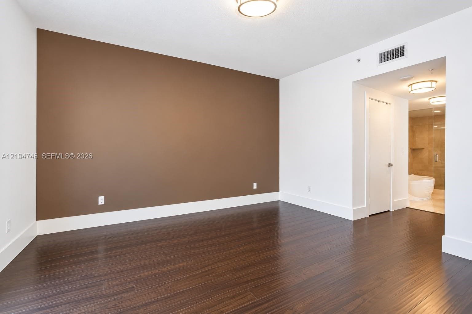 Interior room featuring dark wood-finish flooring, a neutral-toned accent wall, and recessed ceiling lighting