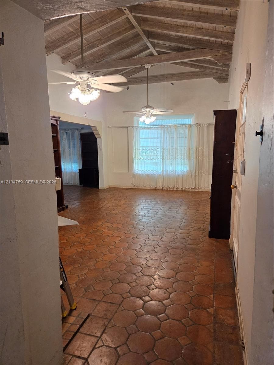 Vaulted ceiling with exposed wood beams, octagonal terracotta tile flooring, and dual ceiling fans with integrated lighting