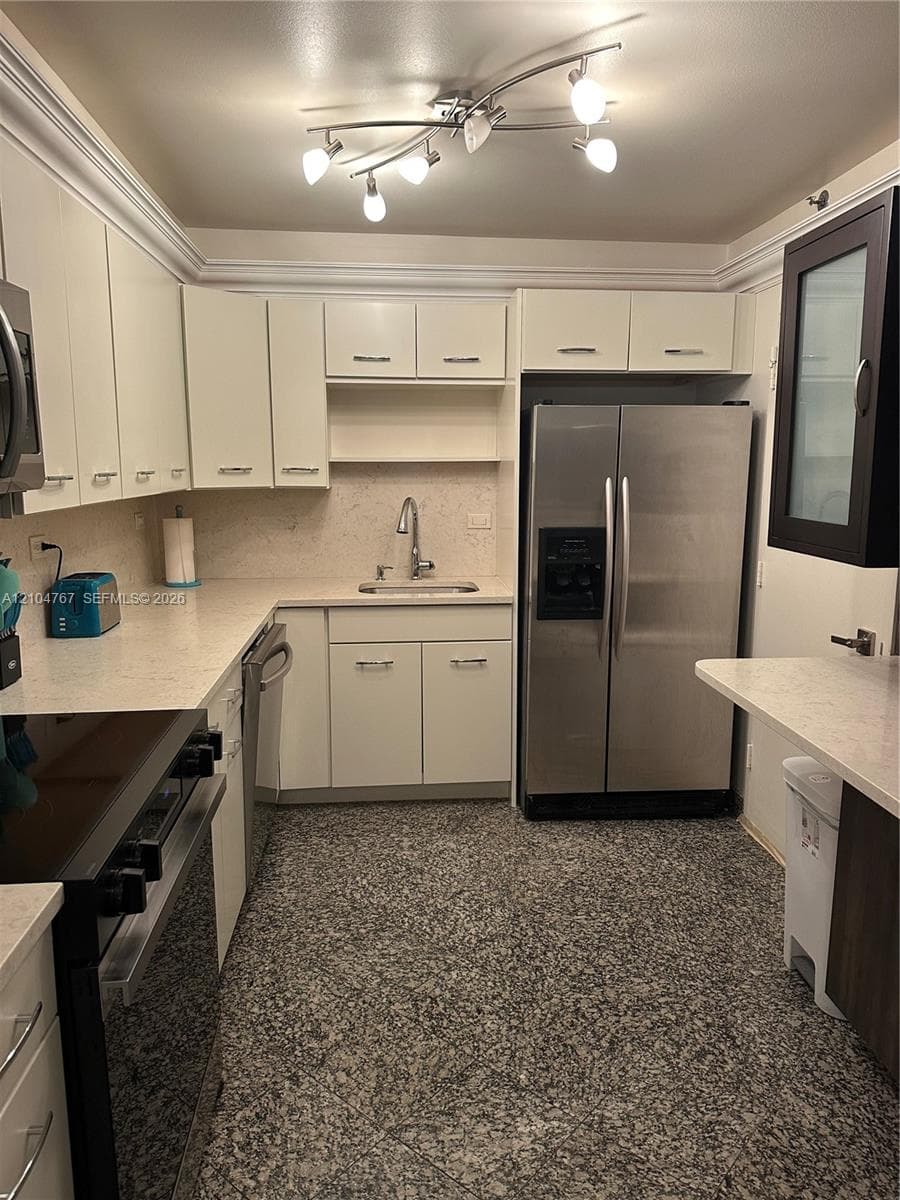 Kitchen featuring white cabinetry, solid surface countertops, stainless steel appliances, a multi-bulb track lighting fixture, and stone-finish flooring