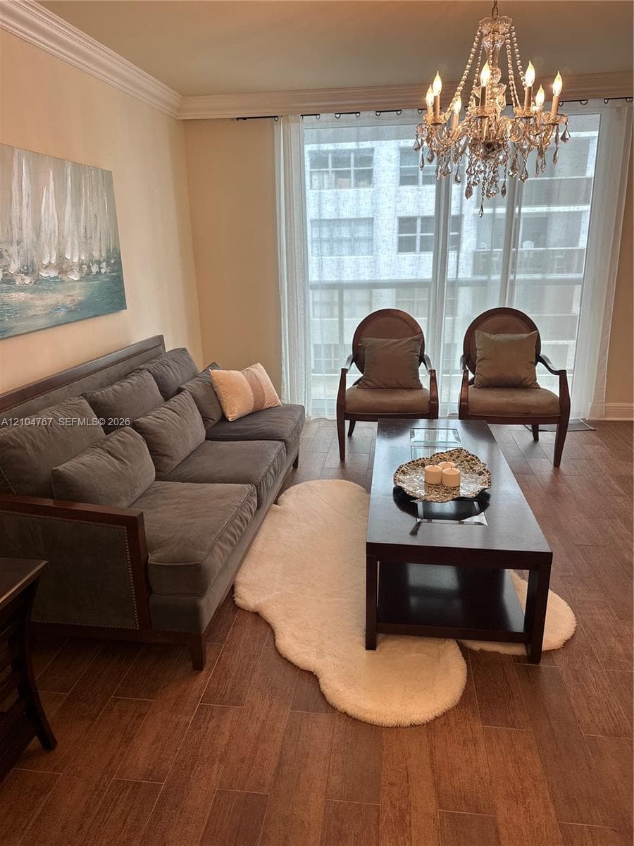 Floor-to-ceiling glass sliding doors, wood-finish flooring, crystal chandelier, and crown molding