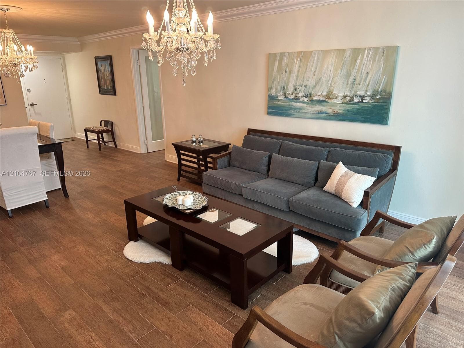 Open living area featuring wood-finish flooring, crown molding, and two decorative crystal chandeliers