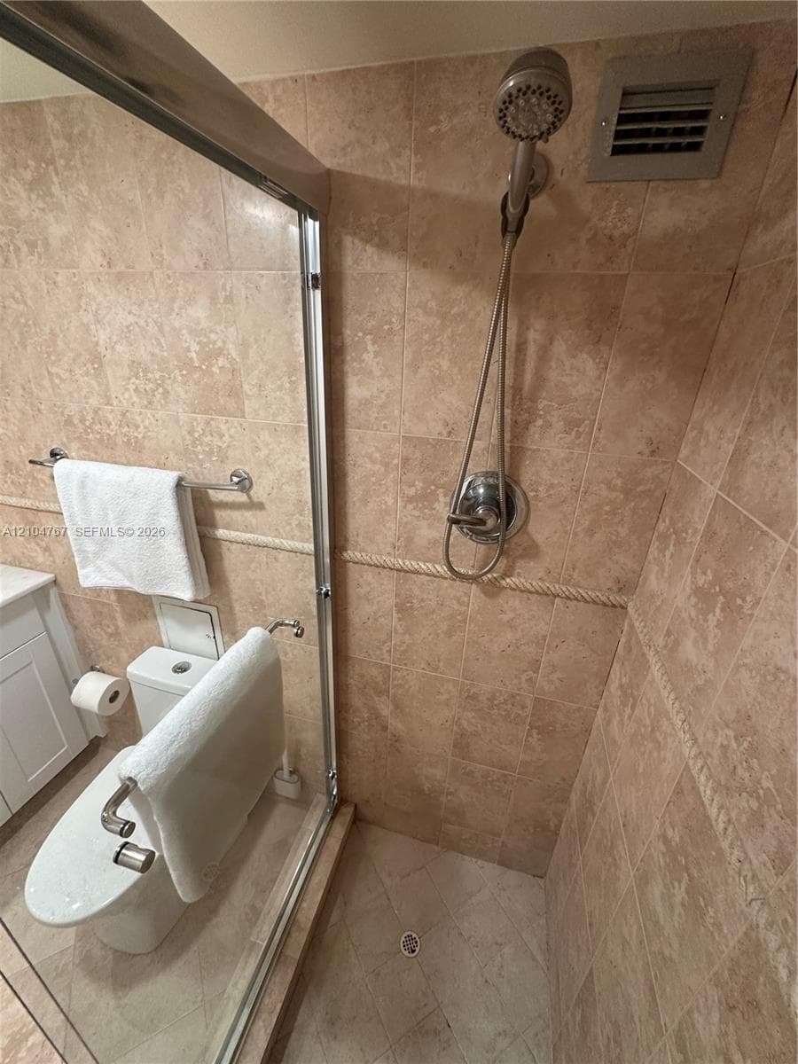 Walk-in shower enclosure featuring full-height stone-finish tile surround with decorative rope trim, adjustable handheld shower head, glass door, and stone-finish floor tile