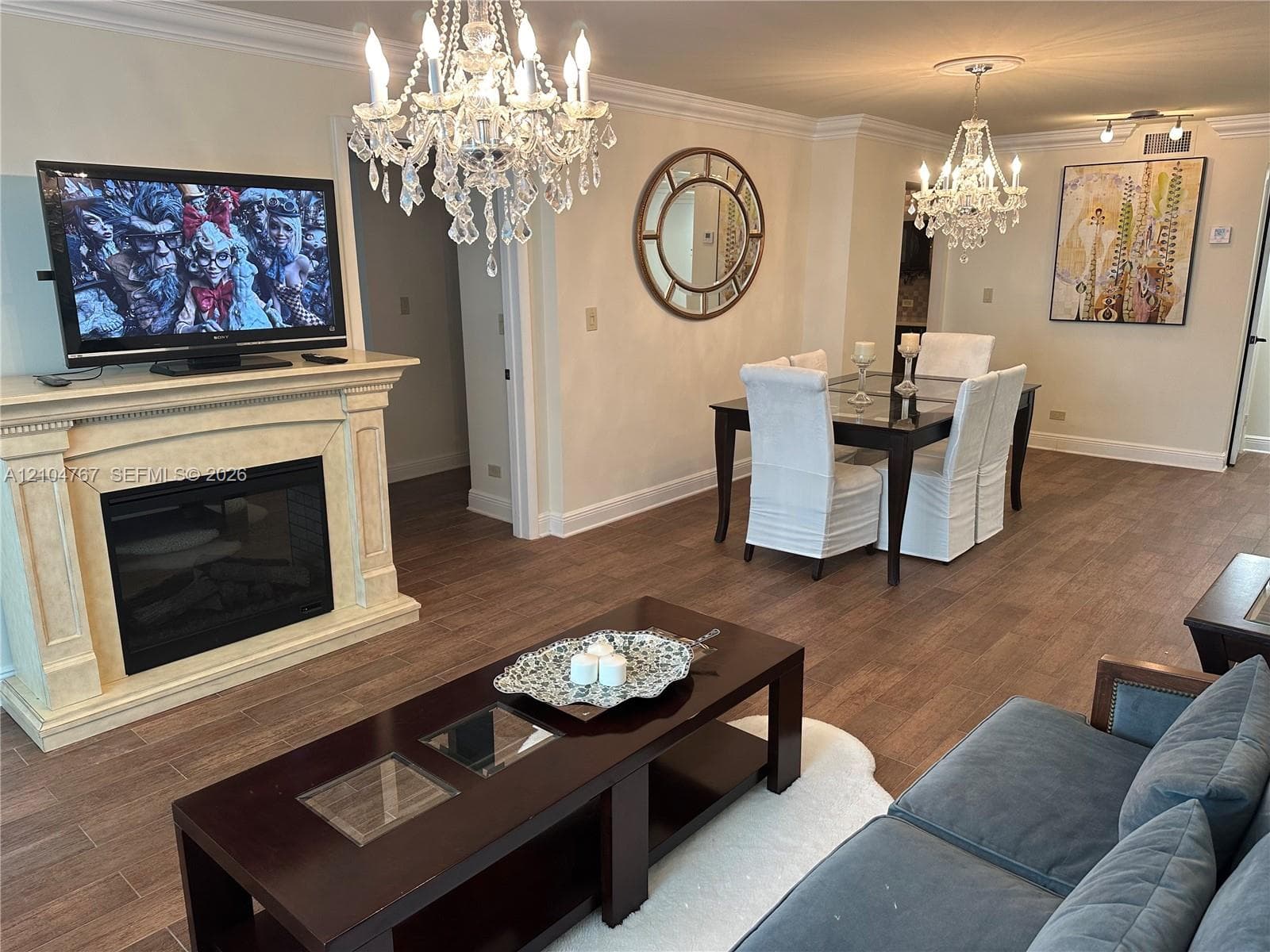 Fireplace with a classical mantel surround, wood-finish flooring, and multiple crystal chandeliers