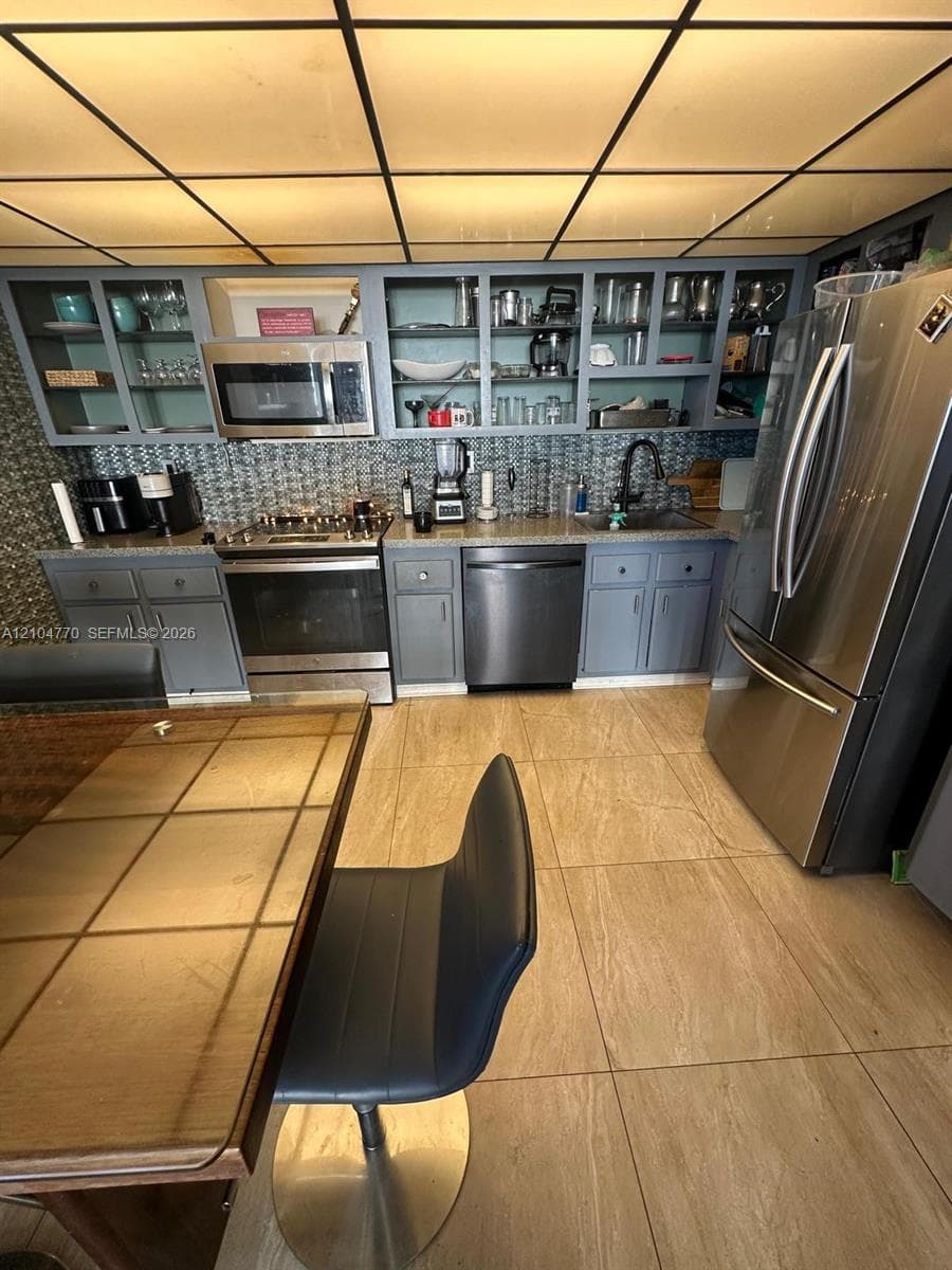 Kitchen featuring stainless steel appliances, grey cabinetry, a patterned tile backsplash, and light-toned floor tiling