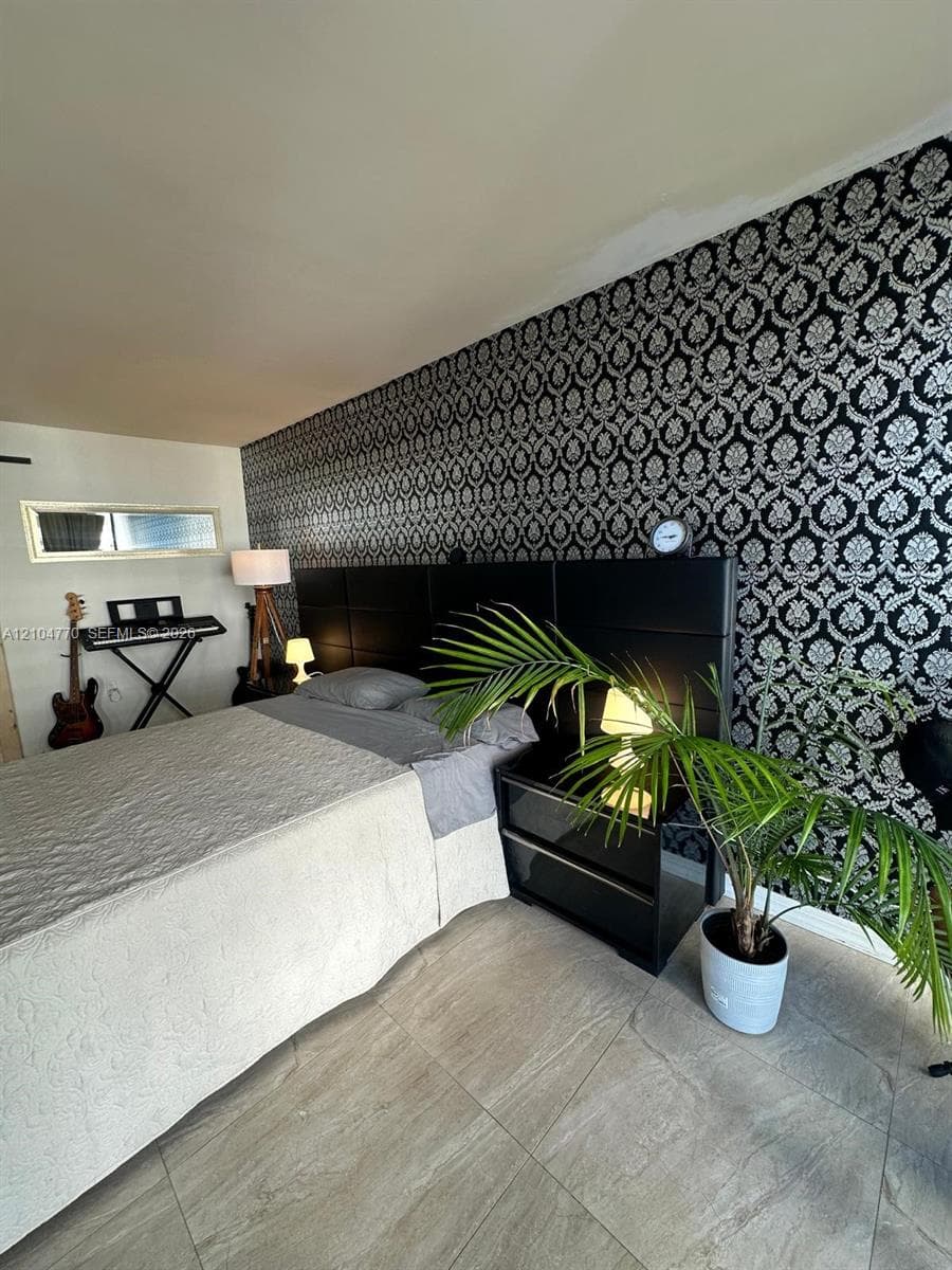 Wood-finish tile flooring, black paneled headboard, patterned accent wall, recessed window, and a built-in lamp