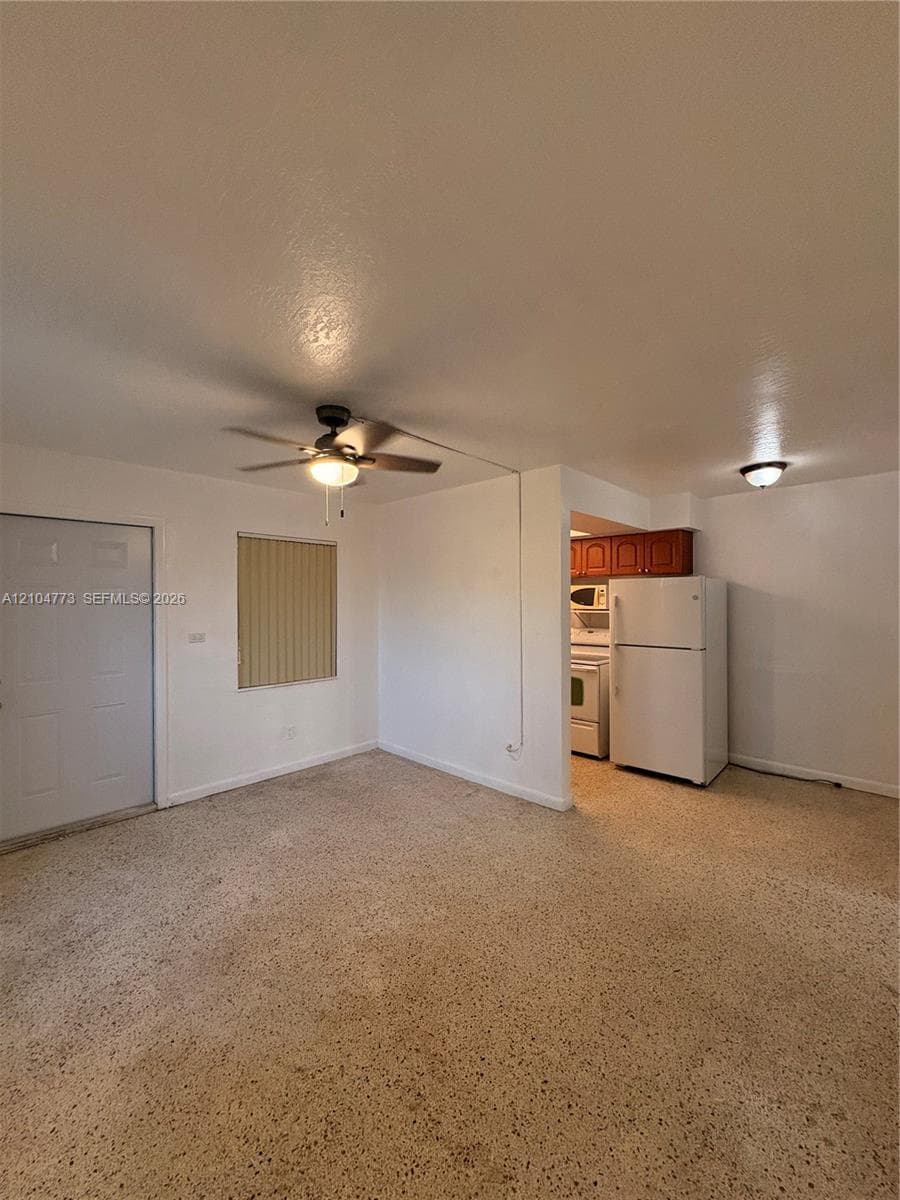 Textured flooring, a ceiling fan with integrated lighting, and a window with horizontal blinds