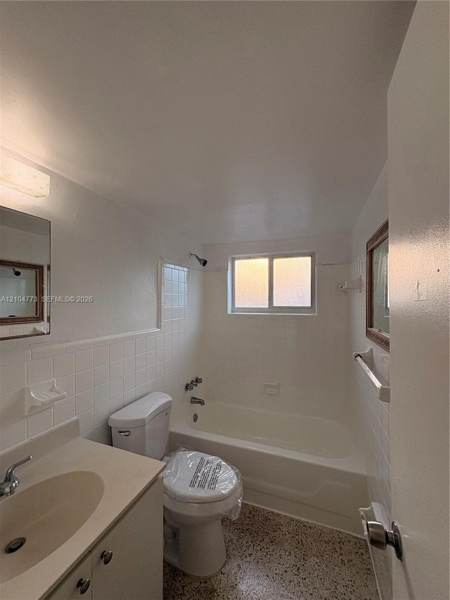 Bathroom featuring a single vanity, integrated sink, and white ceramic tile tub surround