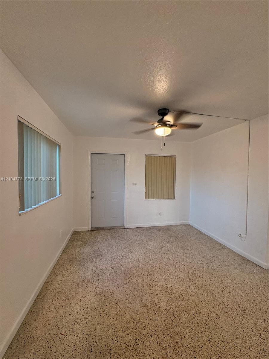Neutral wall paint with textured flooring, a ceiling fan with integrated lighting, and horizontal blinds