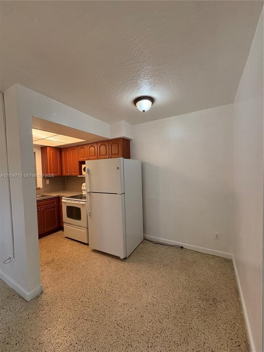 Kitchen with wood-finish cabinetry, tile backsplash, and white appliances