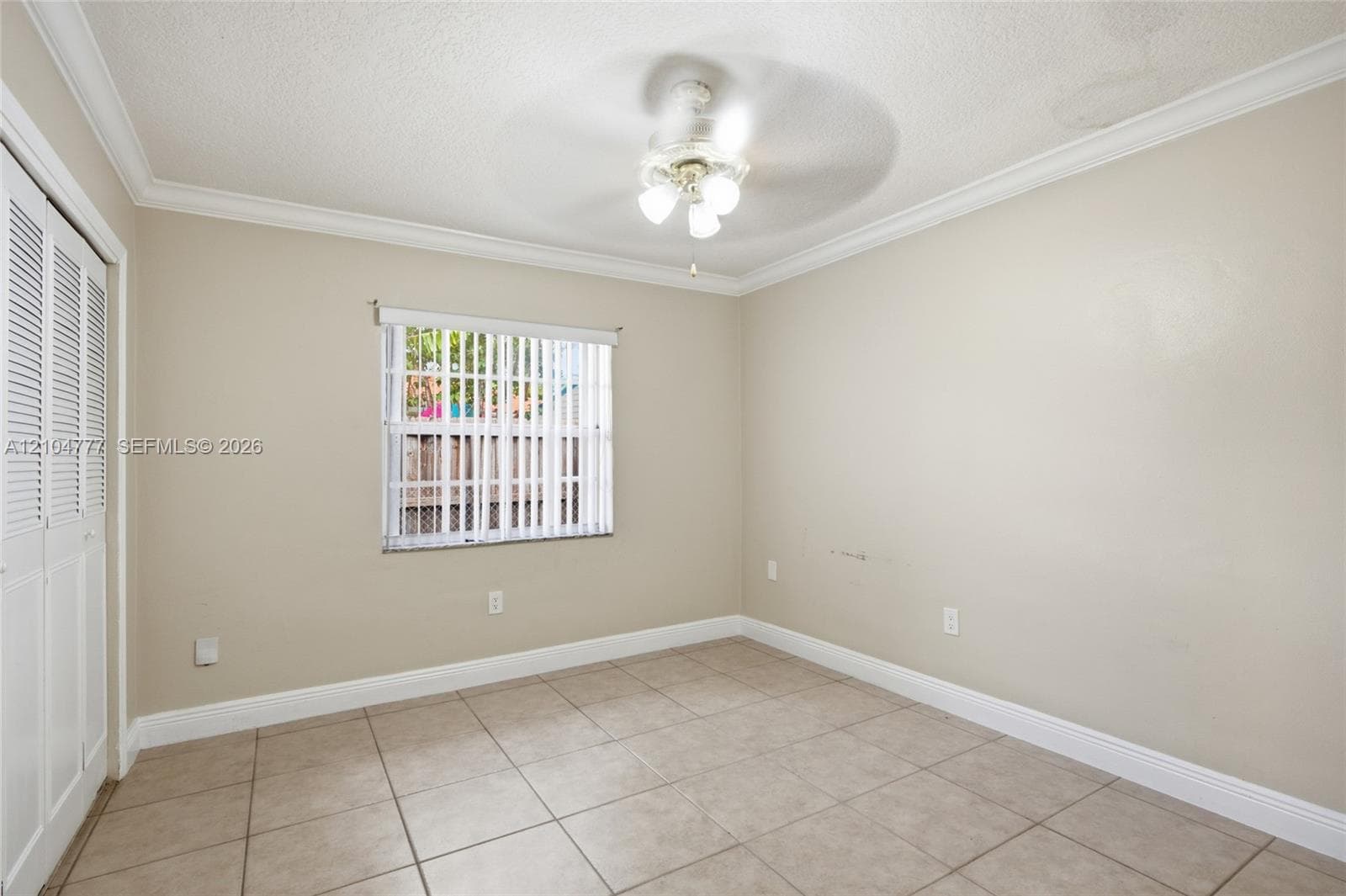 Neutral tone walls, crown molding, ceiling fan with integrated lighting, tiled flooring, and louvered closet doors