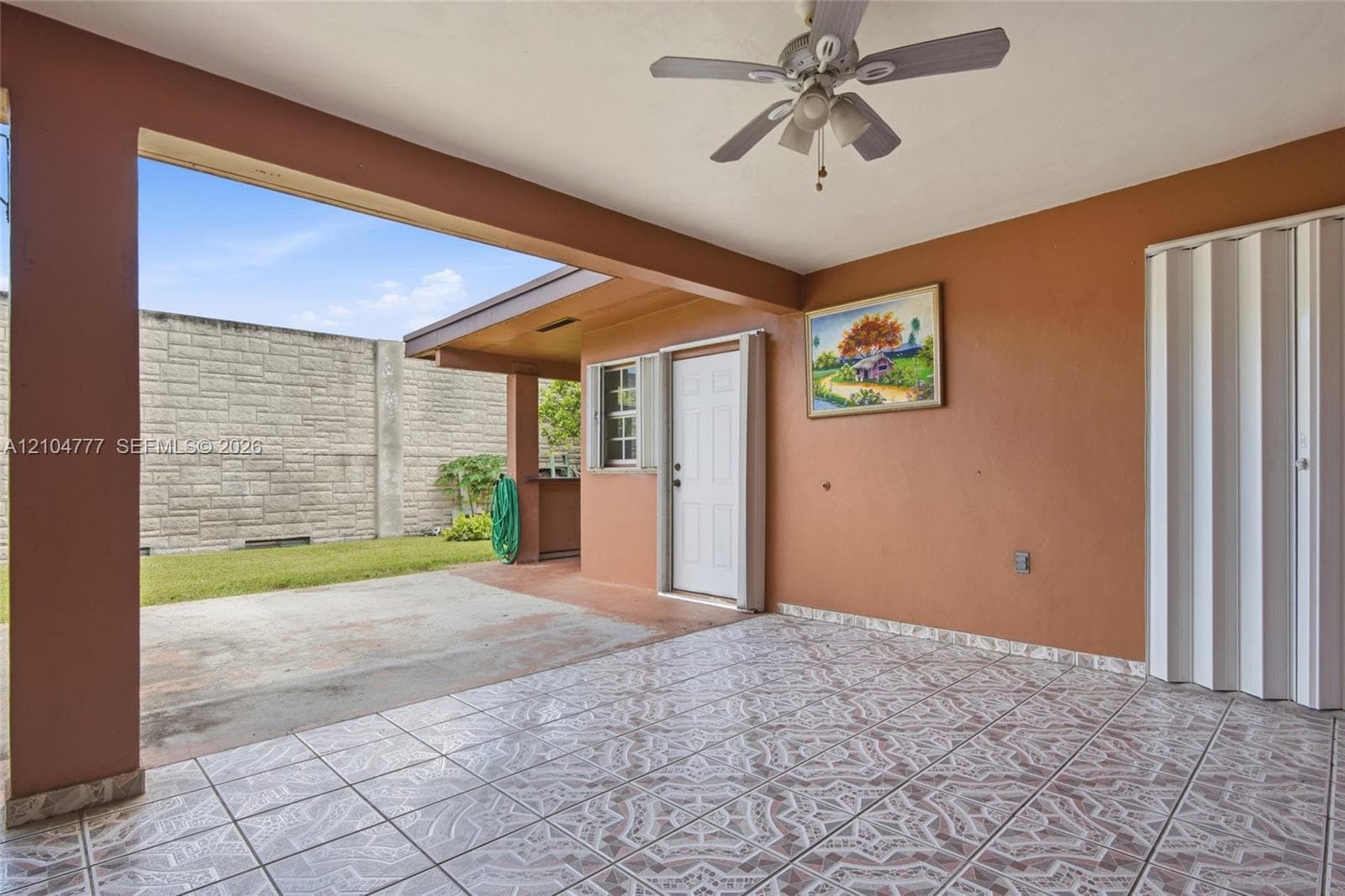 Covered patio featuring patterned tile flooring, a ceiling fan with light, and a privacy wall