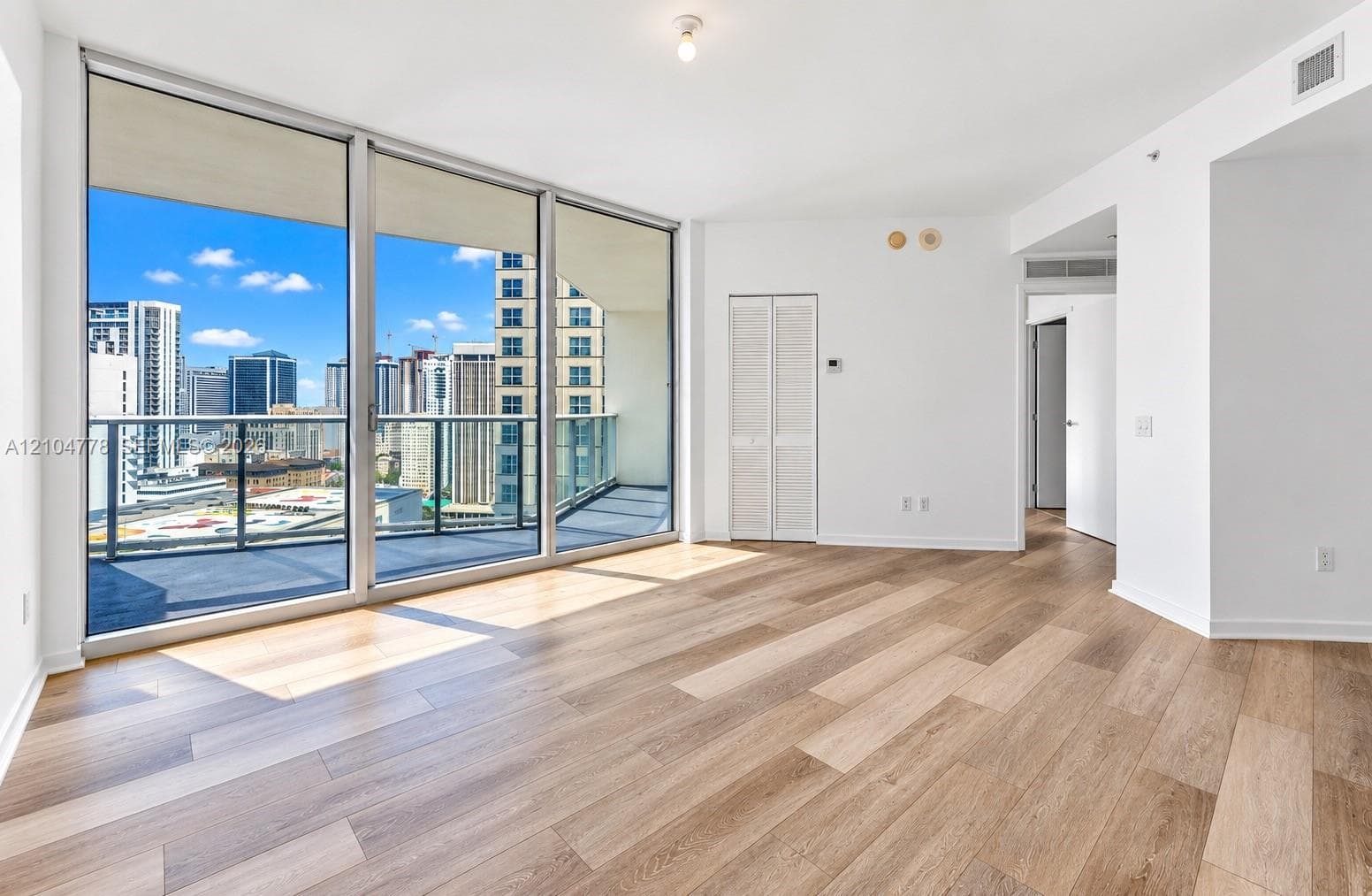 Expansive sliding glass doors, private balcony, wood-finish flooring, white painted walls, and a ceiling-mounted light fixture